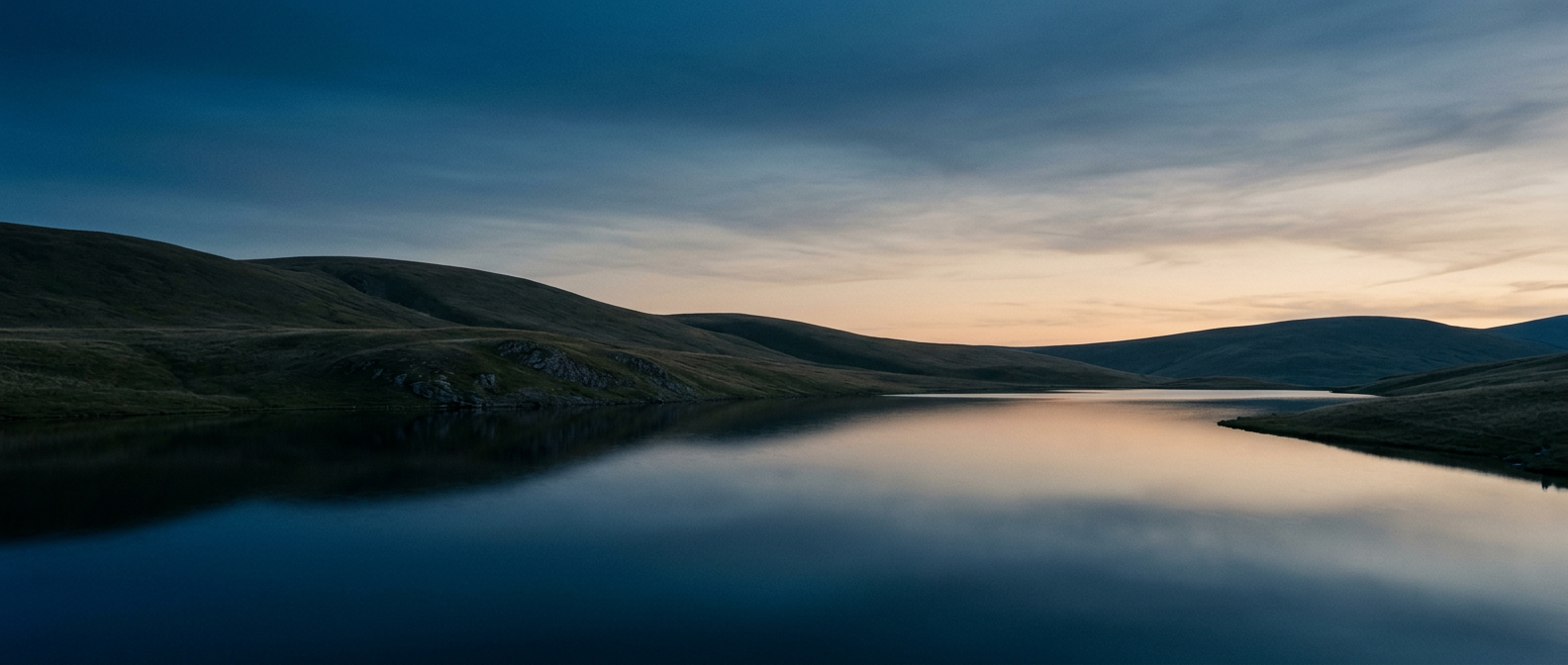 Dusk over rolling hills and a still lake, in deep blue and beige tones